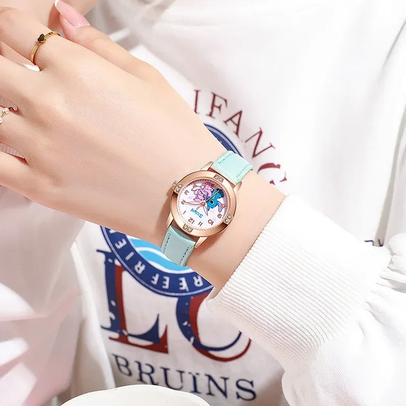 Hand wearing a light blue watch with a decorative face, against a blurred background with visible text.