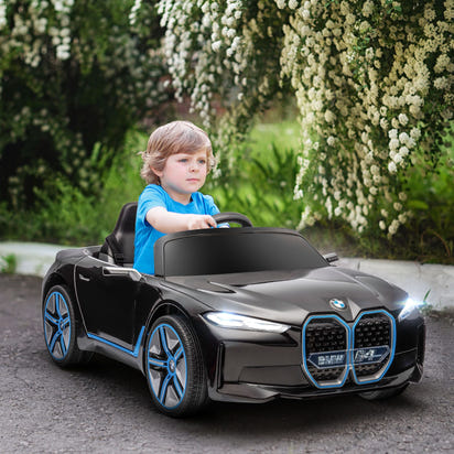Child driving a toy BMW car on a path with greenery and flowers in the background