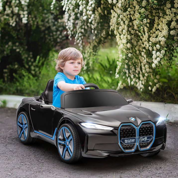 Child driving a toy BMW car on a path with greenery and flowers in the background