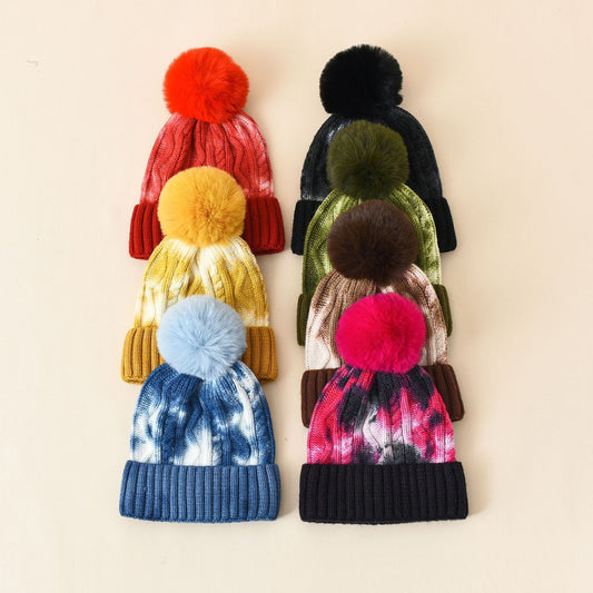 Set of colorful knit hats with pom-poms on a beige background