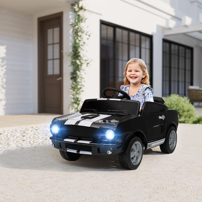 Child sitting in a black toy car with glowing headlights in front of a house.