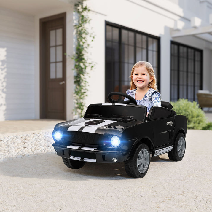 Child sitting in a black toy car with glowing headlights in front of a house.