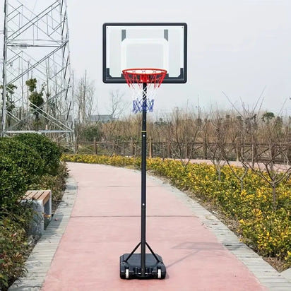 Basketball hoop on a stand outdoors with a pathway and greenery in the background