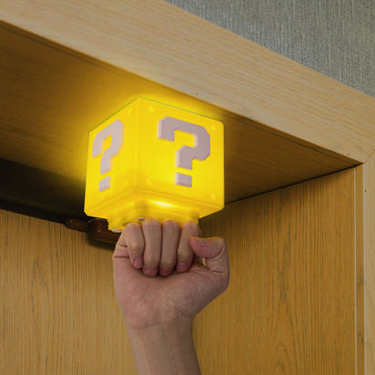 Hand holding a yellow cube with question marks under a wooden shelf.