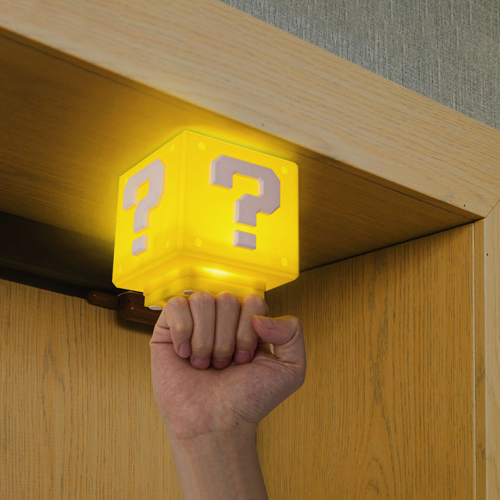 Hand holding a yellow cube with question marks under a wooden shelf.