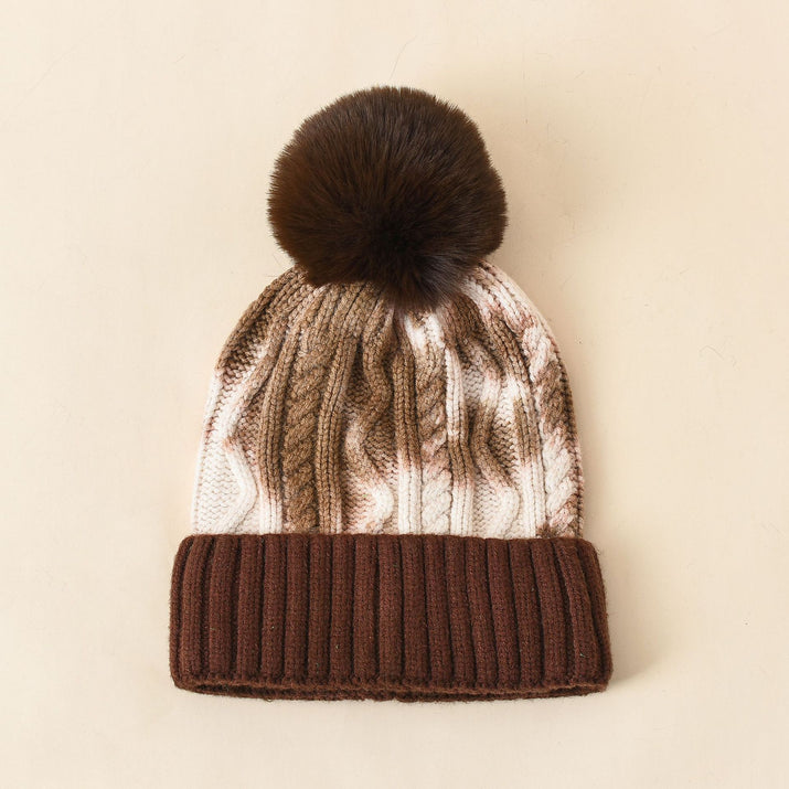 Knitted beanie with brown ribbed band and fur pom-pom on a beige background