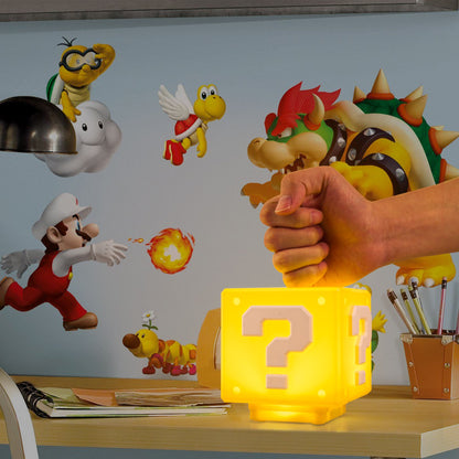 Hand holding a yellow lamp with a question mark, surrounded by cartoon characters on a wall.