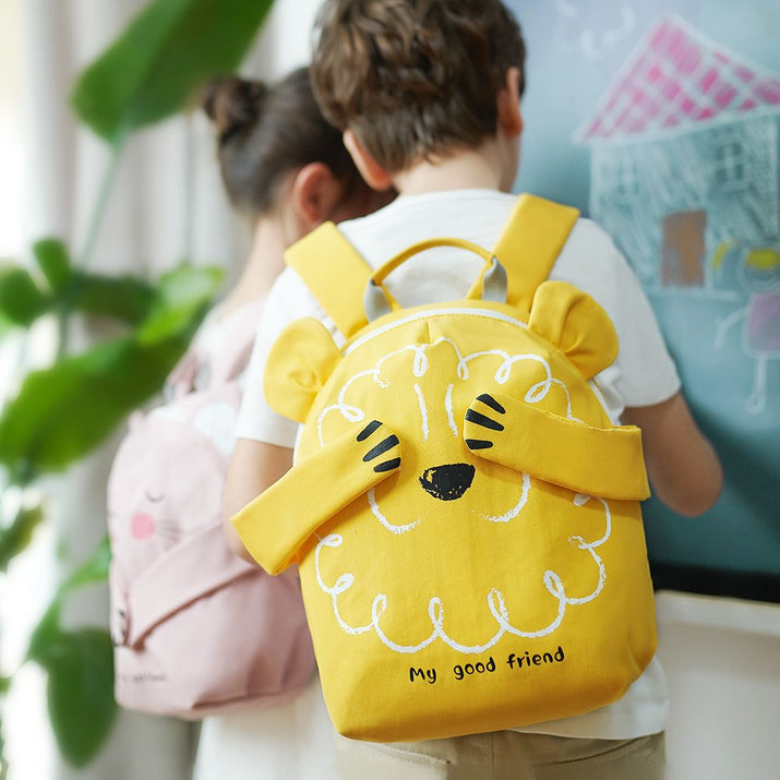 Child wearing a yellow backpack with a cartoon design, standing in front of a colorful wall.